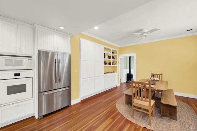 kitchen with white appliances, built in features, white cabinetry, ornamental molding, and dark hardwood / wood-style flooring