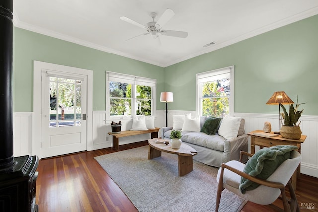 living room featuring dark wood-type flooring, ceiling fan, ornamental molding, and a wood stove