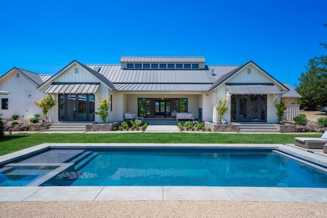 rear view of property featuring a standing seam roof, a yard, an outdoor pool, and metal roof