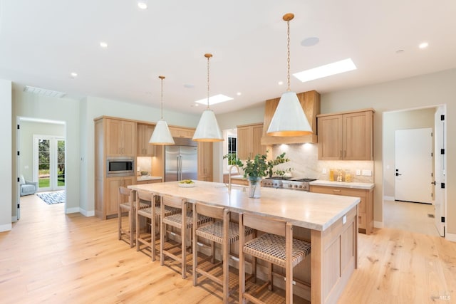 kitchen featuring light brown cabinets, premium range hood, a large island with sink, built in appliances, and tasteful backsplash