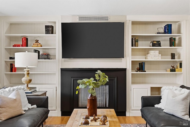 living room with a fireplace, built in features, and light wood-type flooring