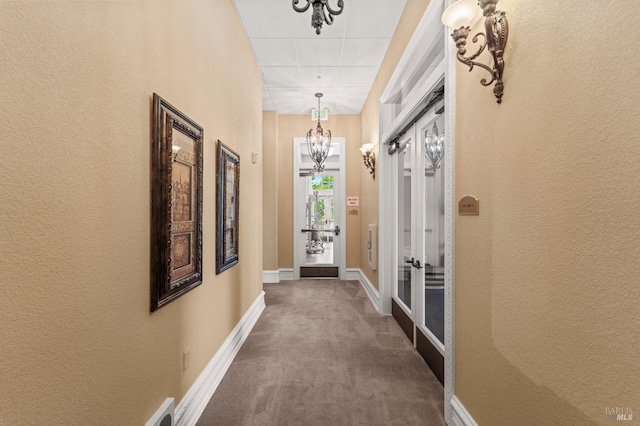 hallway with carpet, a chandelier, baseboards, and a textured wall