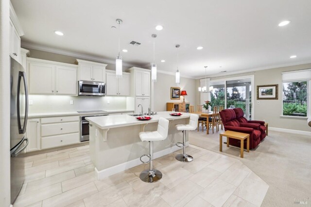 kitchen featuring white cabinetry, decorative light fixtures, ornamental molding, appliances with stainless steel finishes, and a kitchen island with sink