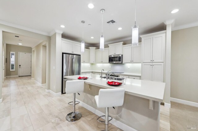 kitchen featuring a kitchen bar, hanging light fixtures, stainless steel appliances, a kitchen island with sink, and white cabinets