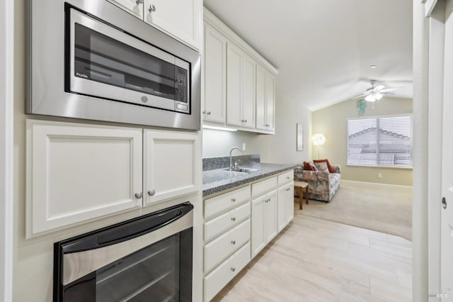 kitchen with vaulted ceiling, stainless steel microwave, white cabinetry, sink, and dark stone countertops