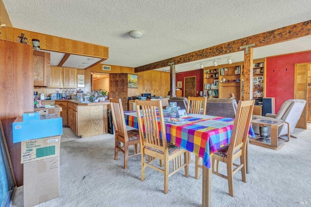 dining room with visible vents, light colored carpet, beamed ceiling, a textured ceiling, and wood walls