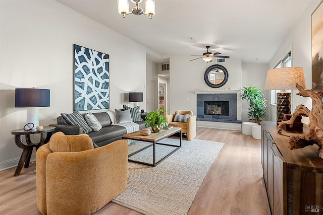 living room with a fireplace, ceiling fan with notable chandelier, and light hardwood / wood-style flooring