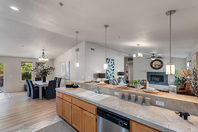 kitchen featuring vaulted ceiling, decorative light fixtures, sink, a tiled fireplace, and stainless steel dishwasher