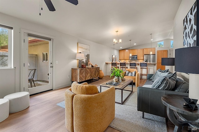 living room with ceiling fan with notable chandelier, plenty of natural light, vaulted ceiling, and light hardwood / wood-style flooring