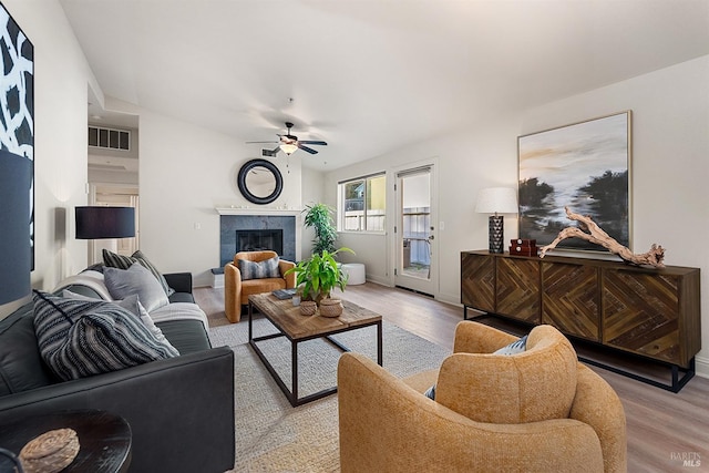 living room with a tile fireplace, ceiling fan, and light wood-type flooring