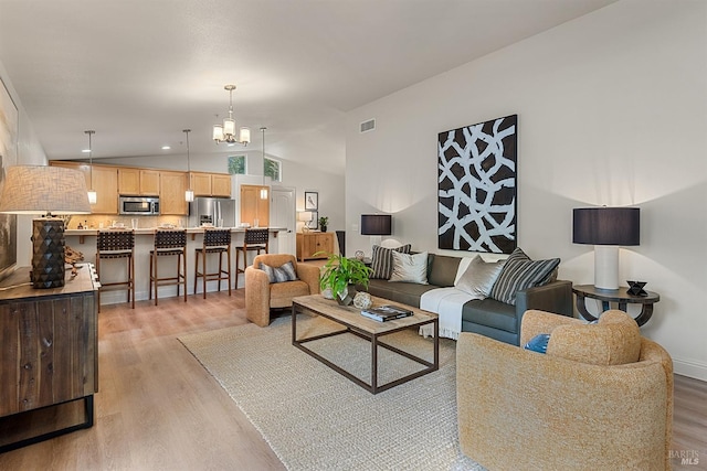 living room with vaulted ceiling, a chandelier, and light hardwood / wood-style floors