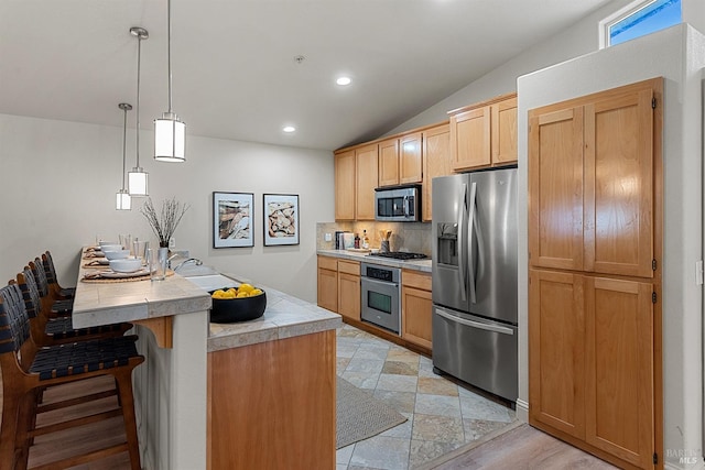 kitchen featuring a breakfast bar, tasteful backsplash, light brown cabinets, appliances with stainless steel finishes, and pendant lighting