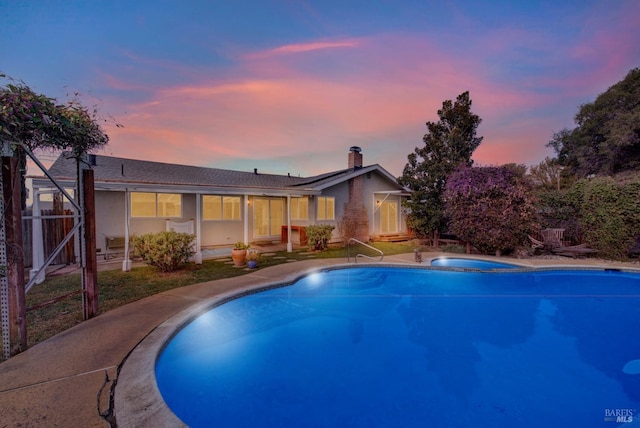 pool at dusk with an in ground hot tub