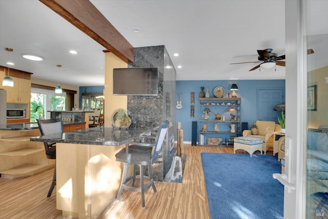 kitchen with hanging light fixtures, light wood-type flooring, a large fireplace, kitchen peninsula, and beamed ceiling