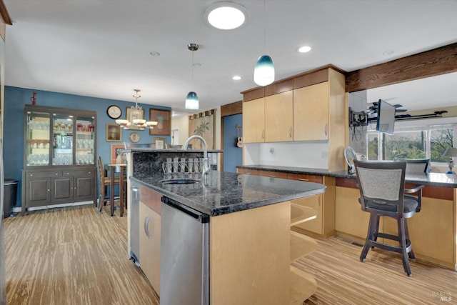 kitchen featuring sink, an island with sink, decorative light fixtures, dark stone counters, and light brown cabinets