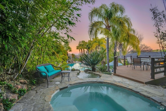 pool at dusk with a wooden deck and a hot tub