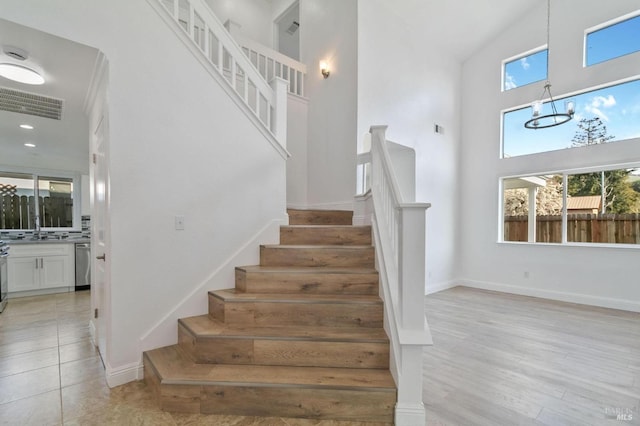 stairway featuring an inviting chandelier, a towering ceiling, wood-type flooring, and sink