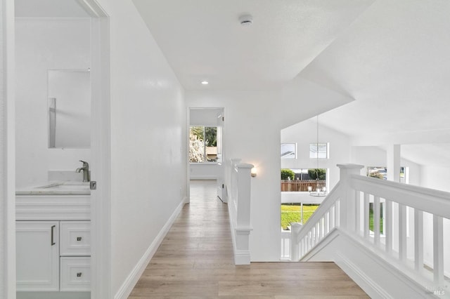 corridor featuring lofted ceiling, sink, and light hardwood / wood-style flooring