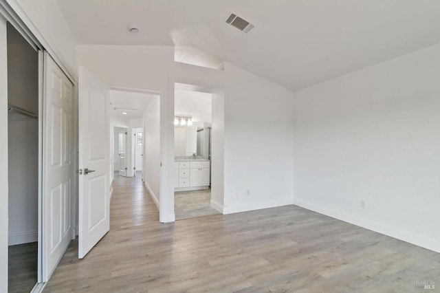 unfurnished bedroom with a closet, lofted ceiling, connected bathroom, and light hardwood / wood-style flooring