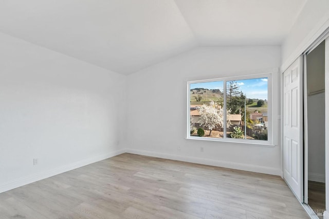 unfurnished bedroom with vaulted ceiling, light hardwood / wood-style floors, and a closet