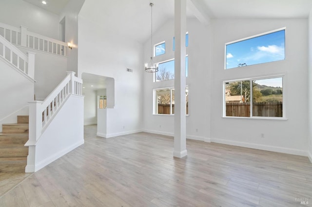 unfurnished living room featuring a notable chandelier, beam ceiling, light hardwood / wood-style flooring, and high vaulted ceiling