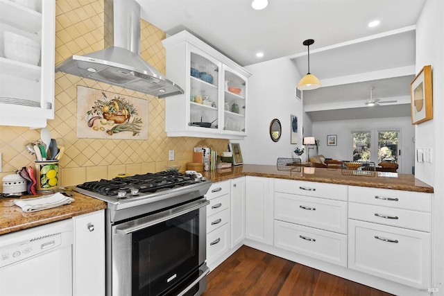 kitchen with white cabinetry, stainless steel range with gas stovetop, white dishwasher, dark stone counters, and wall chimney exhaust hood