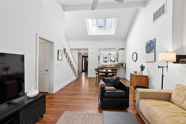 living room featuring wood-type flooring, a skylight, high vaulted ceiling, ceiling fan, and beam ceiling