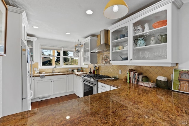 kitchen with white cabinets, gas range, dark stone counters, wall chimney exhaust hood, and white fridge