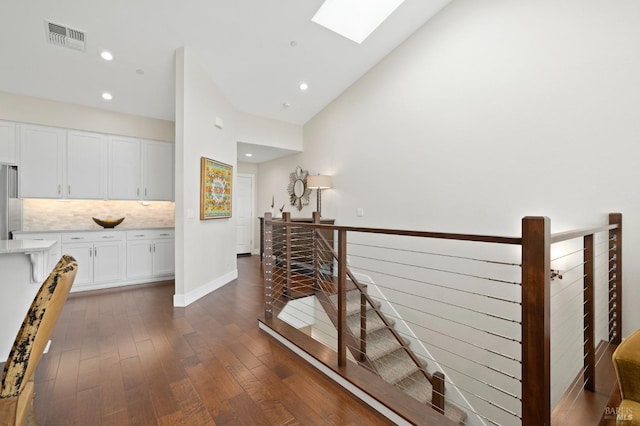 corridor with lofted ceiling with skylight, visible vents, recessed lighting, an upstairs landing, and dark wood-type flooring