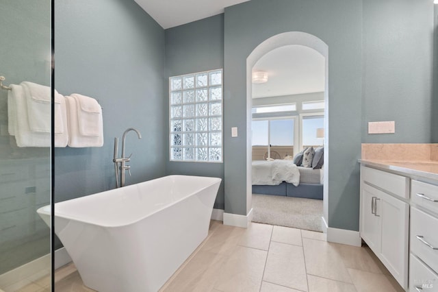 ensuite bathroom with a freestanding bath, baseboards, vanity, and connected bathroom