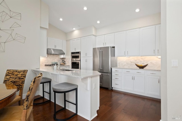 kitchen featuring a sink, under cabinet range hood, appliances with stainless steel finishes, white cabinetry, and a peninsula