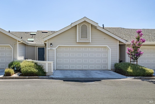 ranch-style home featuring an attached garage, roof with shingles, solar panels, and driveway