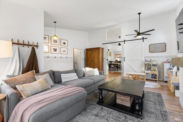 living room featuring ceiling fan, high vaulted ceiling, a barn door, and hardwood / wood-style floors