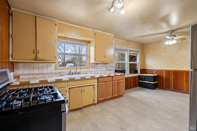 kitchen featuring sink, stainless steel gas stove, tasteful backsplash, tile countertops, and wood walls