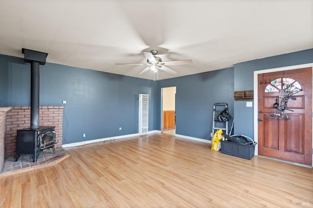 foyer entrance with ceiling fan, a wood stove, and light hardwood / wood-style floors