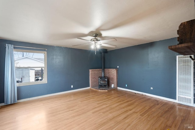 unfurnished living room featuring ceiling fan, a wood stove, and light hardwood / wood-style floors