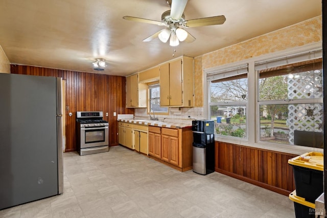 kitchen with ceiling fan, appliances with stainless steel finishes, sink, and wood walls