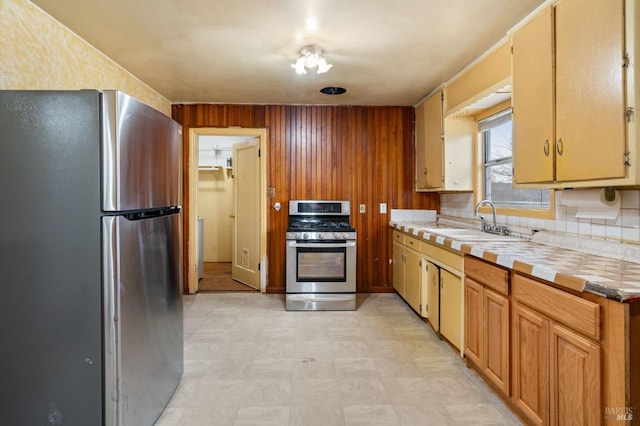 kitchen featuring sink, appliances with stainless steel finishes, wooden walls, tile counters, and backsplash