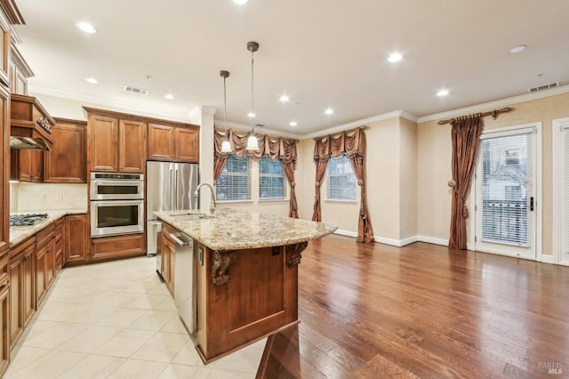 kitchen with crown molding, appliances with stainless steel finishes, a center island with sink, and decorative light fixtures