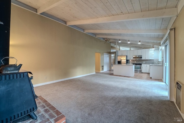 unfurnished living room featuring sink, a wood stove, vaulted ceiling with beams, ceiling fan, and light carpet