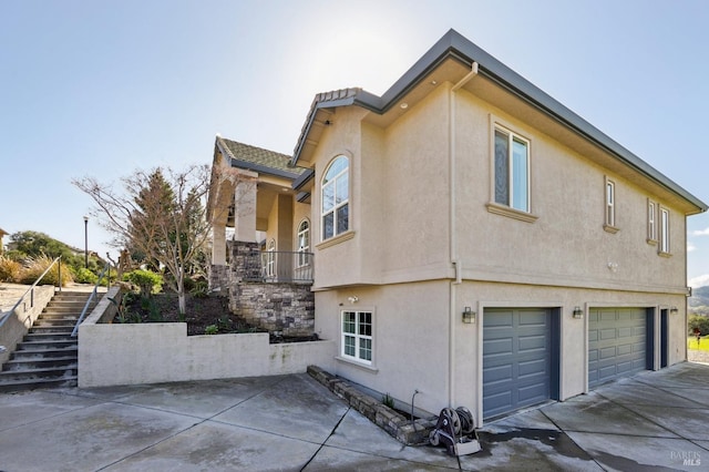 view of property exterior featuring a garage, concrete driveway, stairway, and stucco siding