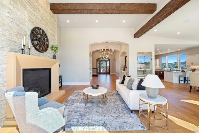 living room featuring beam ceiling, a fireplace, a chandelier, and light wood-type flooring