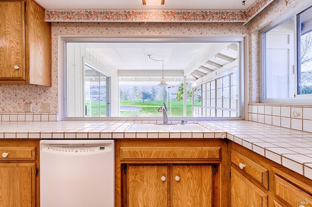 kitchen with tile counters, white dishwasher, sink, and hanging light fixtures