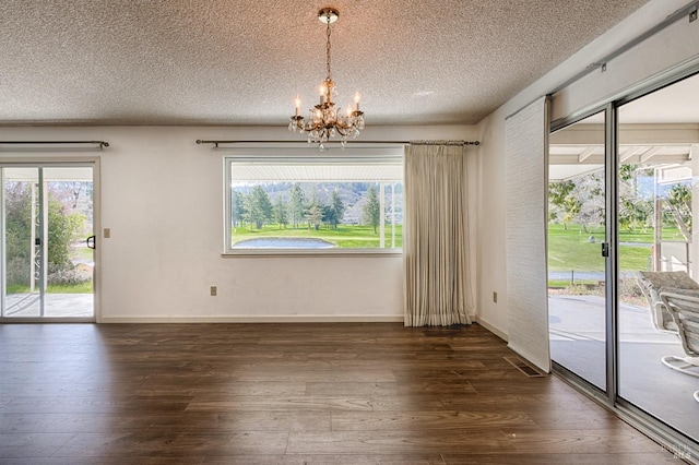 unfurnished dining area with a notable chandelier, dark hardwood / wood-style flooring, a textured ceiling, and a wealth of natural light