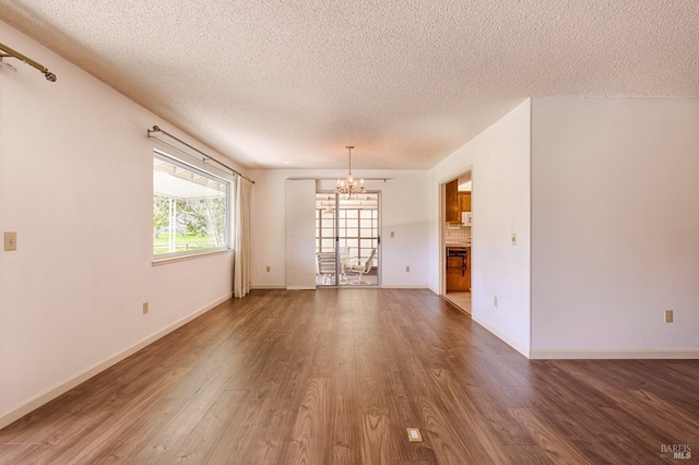 unfurnished living room with dark wood-type flooring, a textured ceiling, and a chandelier