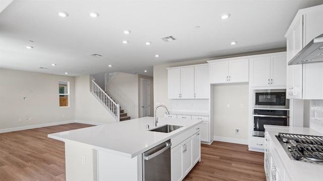 kitchen featuring white cabinets, appliances with stainless steel finishes, a kitchen island with sink, light countertops, and a sink