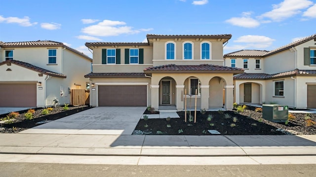 mediterranean / spanish-style home featuring an attached garage, a tile roof, concrete driveway, and stucco siding