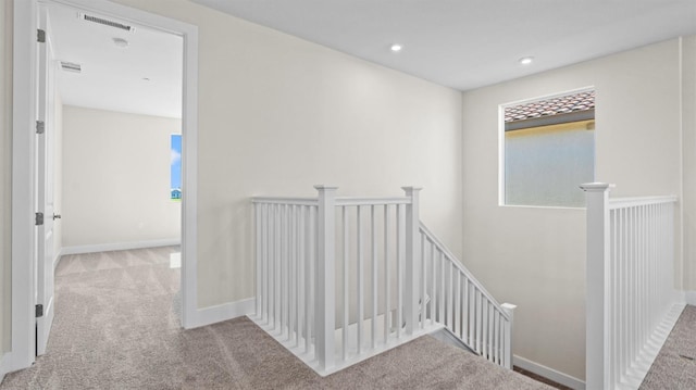 hall with light carpet, baseboards, visible vents, and an upstairs landing