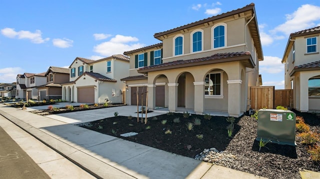 mediterranean / spanish home with driveway, a garage, a tile roof, a residential view, and stucco siding