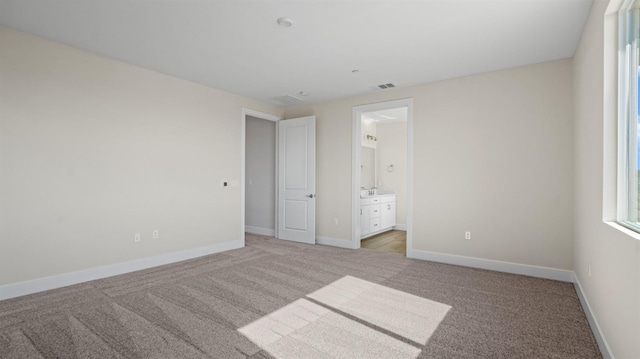 unfurnished bedroom featuring light carpet, ensuite bath, visible vents, and baseboards